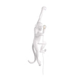 Niori Monkey Hanging Wall Lamp in white resin, sculpted as a monkey suspended by one raised arm while clutching an exposed E27 bulb, with trailing cable.