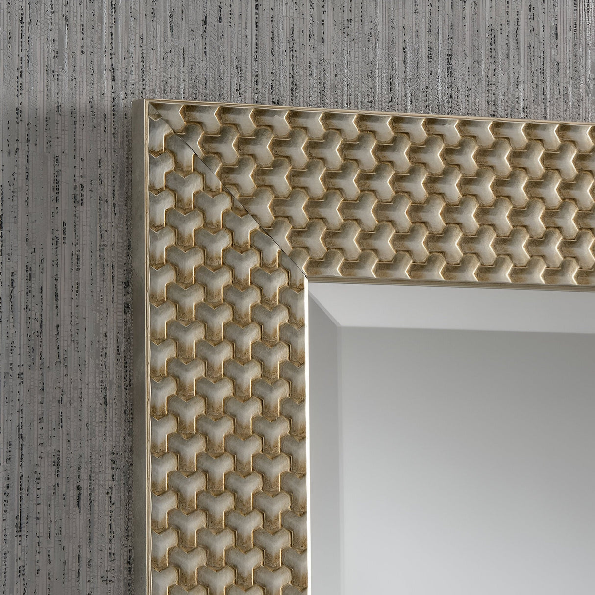 Close-up of the Glimira Rectangle Wall Mirror - Champagne frame highlighting an intricate geometric pattern in rich gold tones. Its champagne finish pairs beautifully with the textured gray wall featuring vertical lines, while the reflection offers a minimal light gray gradient, ideal for elegant home decor.