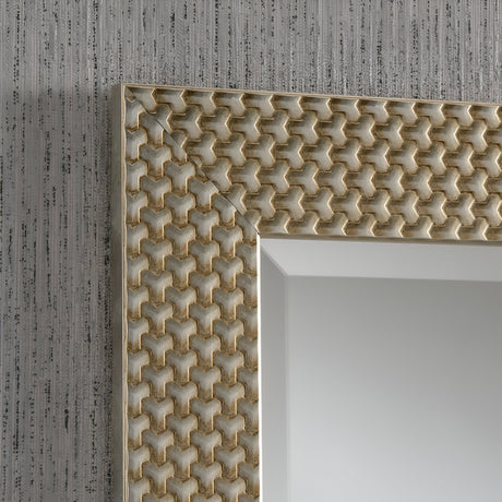 Close-up of the Glimira Rectangle Wall Mirror - Champagne frame highlighting an intricate geometric pattern in rich gold tones. Its champagne finish pairs beautifully with the textured gray wall featuring vertical lines, while the reflection offers a minimal light gray gradient, ideal for elegant home decor.