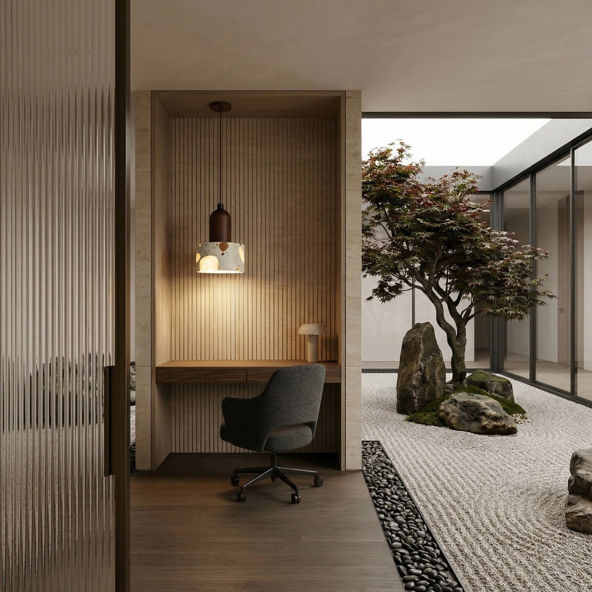 A modern minimalist workspace with a desk and chair set in an alcove features the Terroso 1 Light Drum Travertine Single Pendant Light in Walnut Brown & Light Beige. Glass walls reveal a serene Japanese-inspired zen garden with rocks, gravel, and a tree.