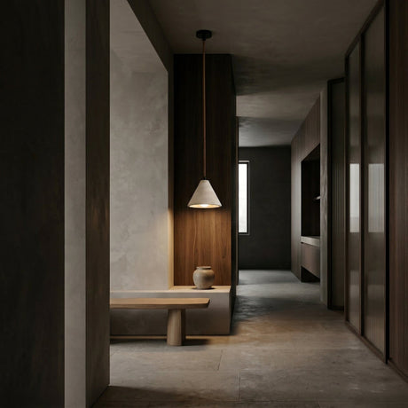 Minimalist hallway with muted tones, featuring a wooden bench, ceramic vase, and wood-paneled walls. Natural light streams through a window, highlighting the Sorella 1 Light Wide Cone Travertine Single Pendant Light in light beige.
