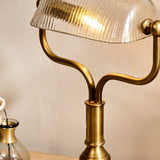 Ulani Vintage Desk Lamp close-up showing ribbed clear glass dome shade on brass ball pivots, twin-stem yoke, and turned antique brass column.