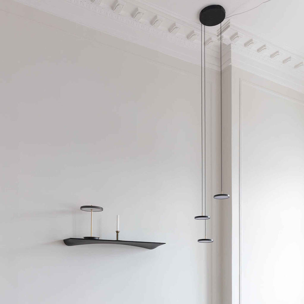 Asteria Micro Cluster Steel Pendant Cord Set with three cords from a black ceiling canopy, holding small round black shades at staggered heights above a wall shelf.