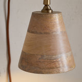 Vattu plug-in wall light with a cone-shaped mango wood shade in banded honey-to-grey tones, antique brass wall plate, and a visible rust-coloured cord.