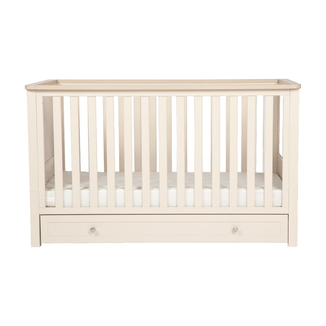 Wanderer Convertible Cot Bed with Drawer in Cashmere, slatted sides with oak-effect top rail, under-bed storage drawer with knob handles, shown on a plain white background.