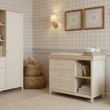 Wanderer Changing Table with Drawers & Removable Top in cashmere, featuring an oak-effect top, three drawers with brushed metal handles, and open side shelving, shown in a nursery setting.