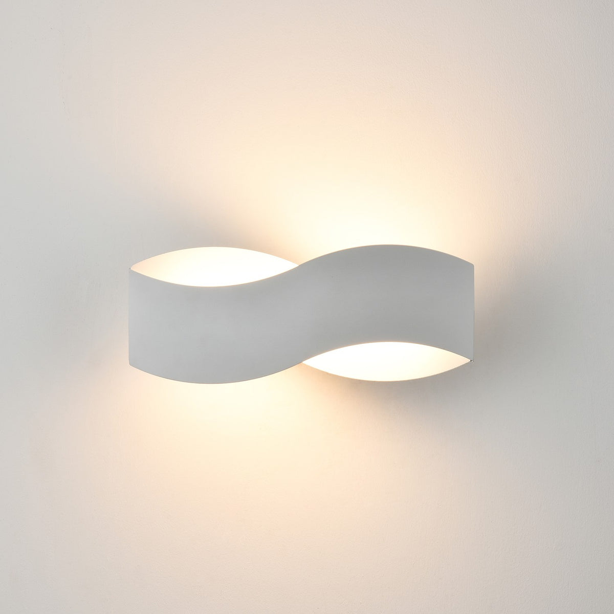 Infinity Matt White LED Wall Light with a curved metal S-shaped body, uplighting and downlighting softly against a plain white wall.