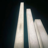 Valmera LED Slim Vertical Alabaster Wall Light in soft white, shown as tall rectangular stone columns of varying heights against a dark background.