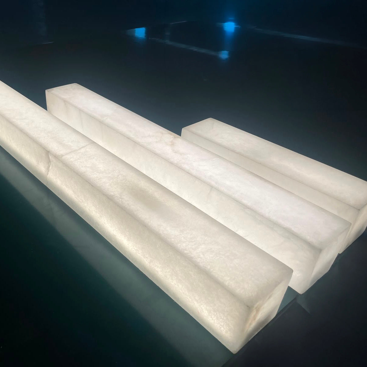 Valmera LED Slim Vertical Alabaster Wall Light in soft white, four rectangular alabaster columns shown lit from within, displayed on a dark reflective surface.