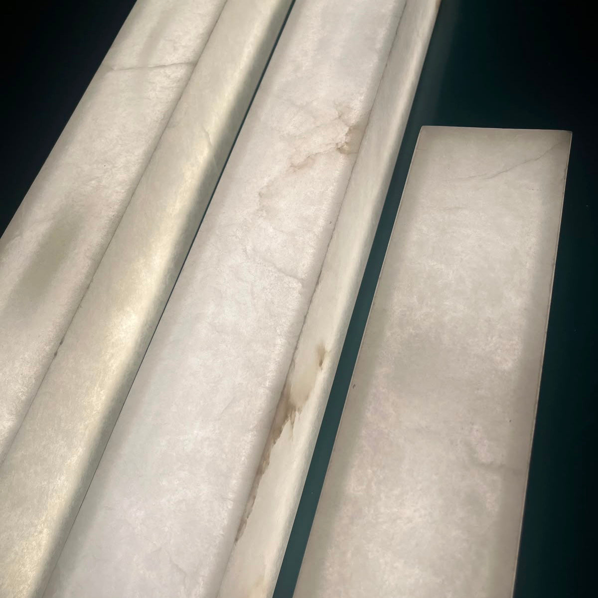Valmera LED Slim Vertical Alabaster Wall Light in soft white, showing cylindrical and rectangular alabaster stone sections with natural veining against a dark background.
