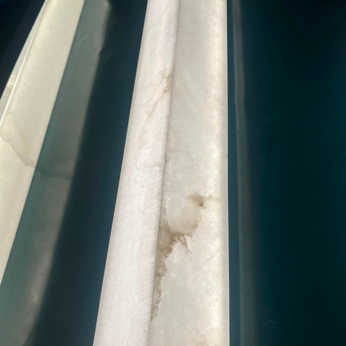 Close-up of the Valmera slim vertical wall light showing the natural veined alabaster column texture in soft white, mounted against a dark background.