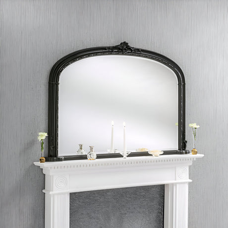 The Brilliance Overmantle Mirror Black - 130x91cm, with its exquisite ornate black frame, is mounted above a white fireplace mantel, adding elegance to the living room decor. Two glowing white candles and small decorative items are thoughtfully arranged on the mantel, perfectly complementing the wall's delicate vertical striped pattern.