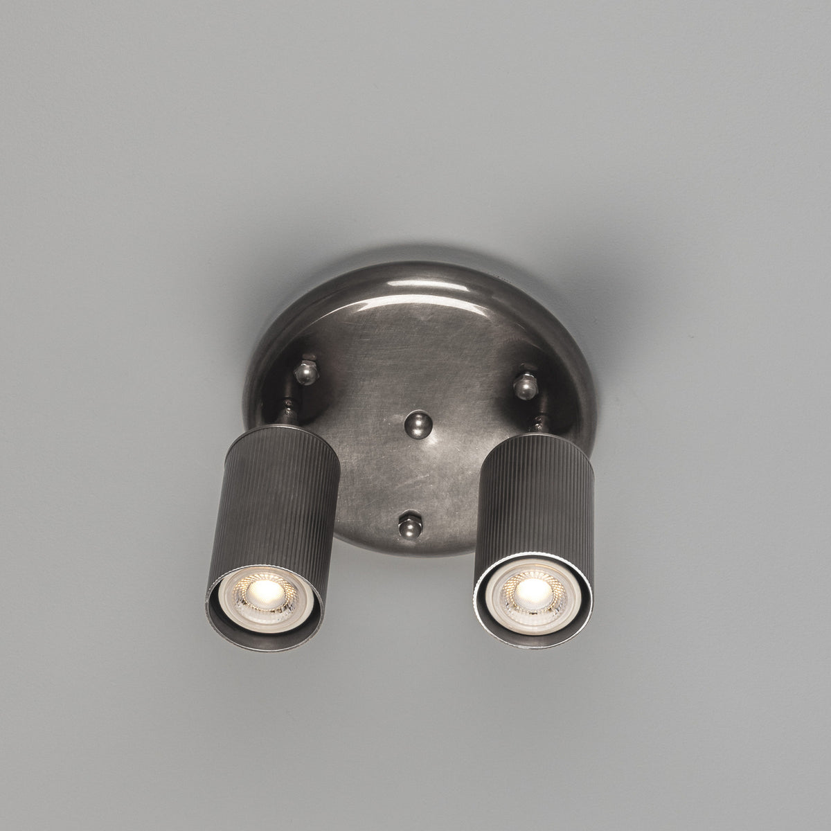 Adare Brass 2 Light Ceiling Spotlight with round ceiling plate, ball finial, and two reeded cylindrical heads on angled arms, shown against a plain grey background.
