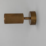 Adare Brass Wall Spotlight with ribbed cylindrical head on a short arm, mounted to a round wall plate in antique brass finish, shown against a plain light grey background.