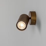 Adare Brass Wall Spotlight with ribbed cylindrical head on a short arm and round wall plate, GU10 bulb lit, shown against a plain grey background.
