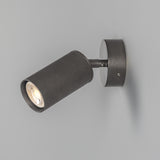 Adare Brass Wall Spotlight with a ribbed cylindrical head on a short arm and round wall plate, finished in dark antique metal, shown on a plain grey background.
