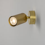 Adare Brass Wall Spotlight with ribbed cylindrical head on a short arm and round wall plate, lit GU10 bulb, shown against a plain light grey background.