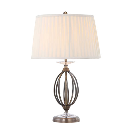 The Aegean Table Lamp - Aged Brass features a metal base in an aged brass finish with an open orb design, complemented by a round, pleated white fabric lampshade. Hand-forged scrolls enhance its elegance as the lamp illuminates with a warm glow.