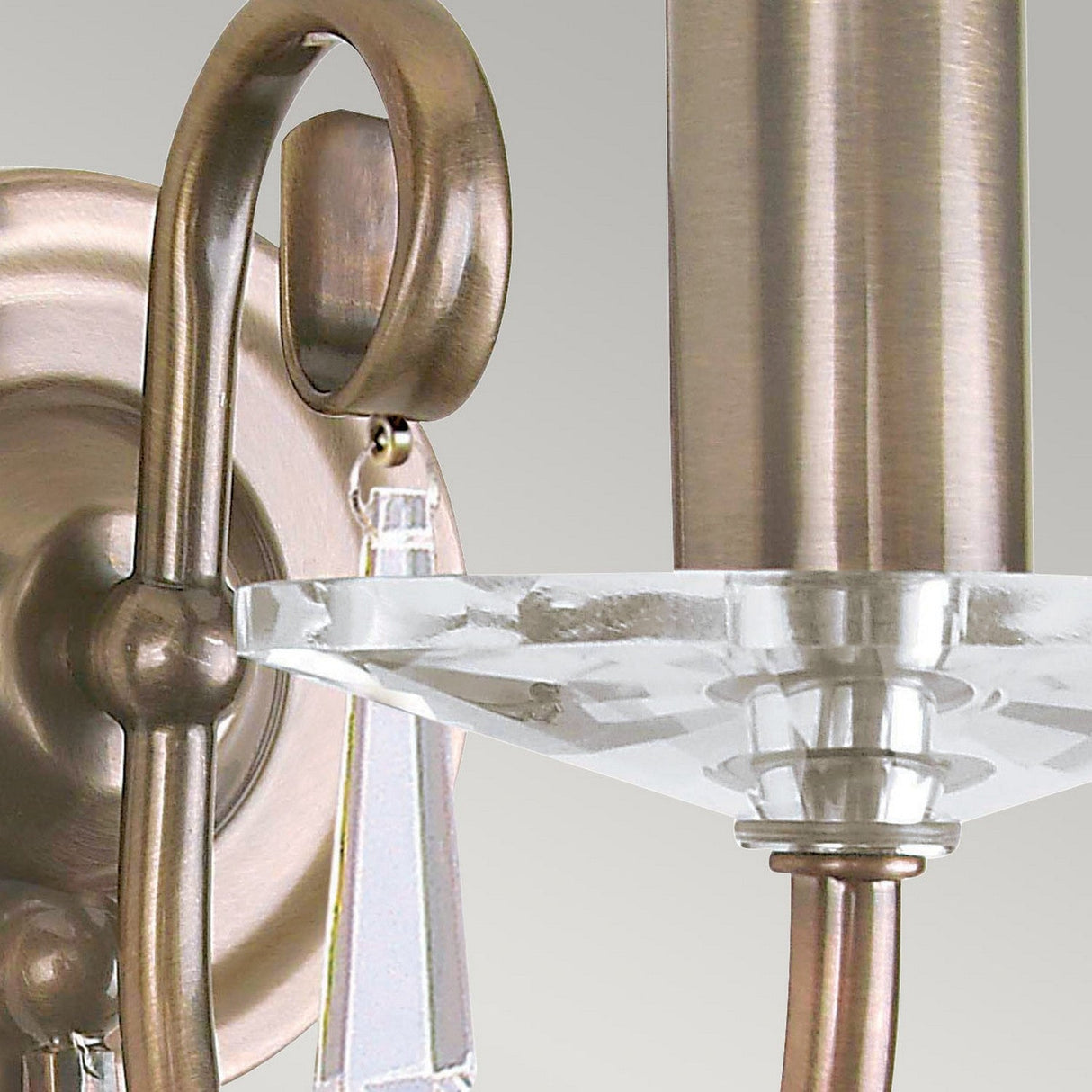 Close-up of the sophisticated Aegean Wall Light in an aged brass finish. This cut glass sconce showcases a curved arm complemented by a clear, faceted glass accent under the bulb holder, set against a simple gray backdrop.