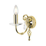 The Aegean Wall Light - Polished Brass is a polished brass sconce with one exposed bulb, crafted to mimic the appearance of a candle. It includes hand-forged scrolls and decorative crystal accents, elegantly mounted on a round brass backing plate with a gracefully curved arm.