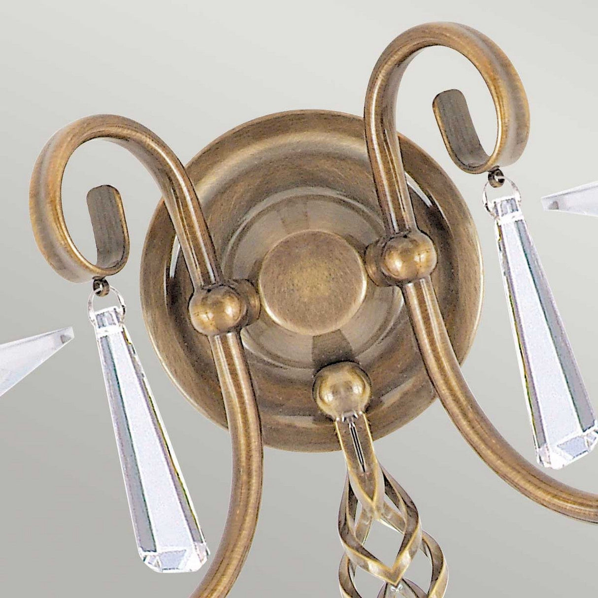 Close-up of the Aegean 2 Light Wall Light in aged brass. It showcases hand-forged scrolls and hanging crystal pendants, adding an elegant touch to the design. The circular light mount beautifully complements the ornate detailing.