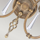 Close-up of the Aegean 2 Light Wall Light in aged brass, showcasing intricately twisted arms and hanging cut-glass droplets, set against a light gray background. The wall light blends classic elegance with a modern touch, highlighted by its hand-forged scrolls.