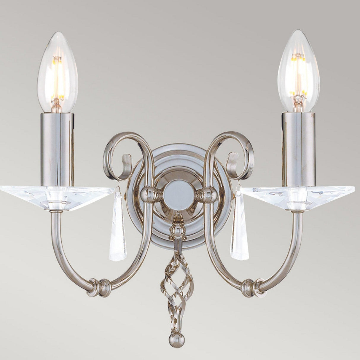 The Aegean 2 Light Wall Light in polished nickel features two arms and candle-shaped bulbs, enhanced by decorative clear prisms, cut-glass droplets, and hand-forged scrolls against a plain gray background.