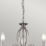 Close-up of the Aegean 3 Light Chandelier - Polished Nickel, showcasing three exposed bulbs. The fixture highlights an intricate open metalwork design with a hanging chain, set against a plain, light-colored wall.