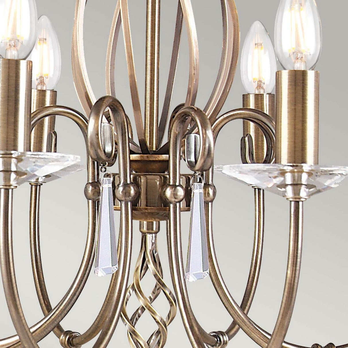 Close-up of the Aegean 8 Light Chandelier in aged brass, showcasing a twisted metal design with candle-shaped bulb holders. Crystal pendants adorn the arms, offering a vintage charm as illuminated bulbs emit a warm glow.