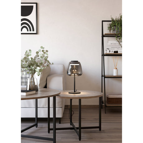 Alfero Smart LED Table Lamp in black, with a slim steel stem and domed smoky glass shade, glowing softly on a side table in a living room setting.