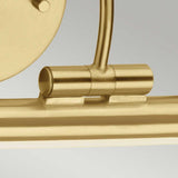 A close-up view of the Alton 1 Light Large LED Picture Light in a brushed brass finish shows its modern metallic hinge attached to a sleek cylindrical rod. The design features smooth lines and a polished surface, reminiscent of Art Display Lighting, with a partial view of its circular component.