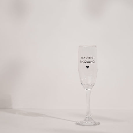 Clear glass champagne flute with a tall slender bowl, long stem and round foot, printed with "BEAUTIFUL bridesmaid" and a small heart, set against a plain light background.