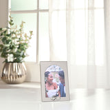 Arch Metal Photo Frame with Linked Rings 6 x 4in in shiny silver, displaying a wedding photo on a white surface near a window with sheer curtains and a potted plant.