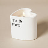 Mr & Mrs Heart Scented Candle in a white ceramic holder with black lower-case lettering, lit wick, heart-shaped rim, on a plain neutral background.
