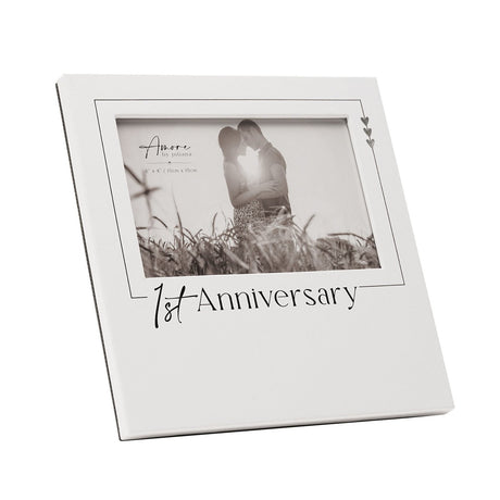 White wooden 6x4in photo frame with "1st Anniversary" printed in black below the picture opening, featuring a fine black border and three small silver hearts in the corner.