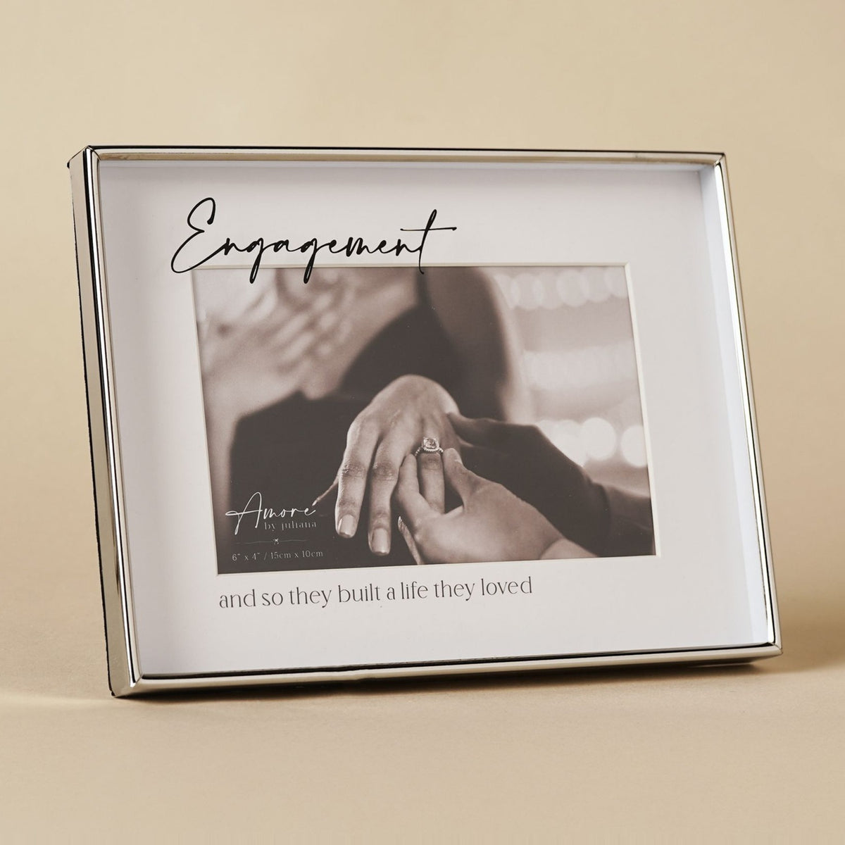 Silver rectangular glass photo frame with "Engagement" in script above a 6 x 4in photo and "and so they built a life they loved" beneath, set on a neutral background.