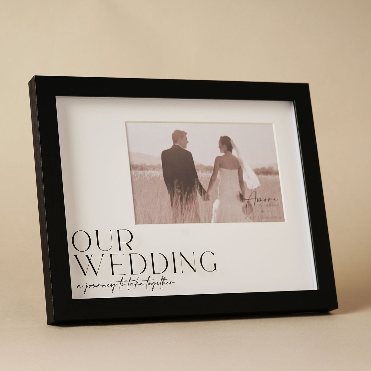 Black wide plastic easel photo frame with "Our Wedding" text and script quote on a white mount, holding a 6 x 4in couple photo, set against a neutral background.