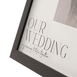 Close-up of the Our Wedding plastic easel photo frame, black woodgrain-effect edge with white mount reading "OUR WEDDING – a journey to take together" above a 6 x 4in photo window.