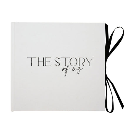 "The Story of Us" textured photo album with white cover, black script lettering, and a black ribbon tie at the open edge, shown on a plain white background.