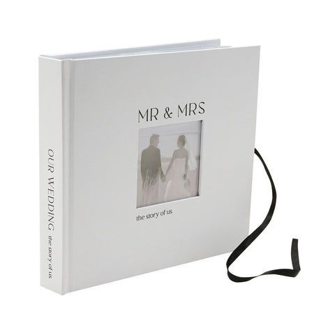 White textured photo album with black ribbon tie, "MR & MRS" and "the story of us" on the cover with a small photo window, "OUR WEDDING" printed on the spine.