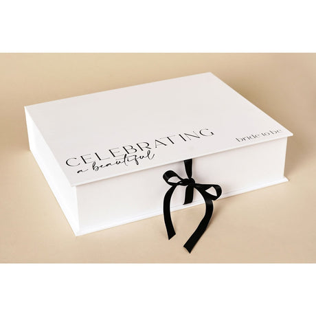 White A4 rectangular keepsake box with black "Celebrating a beautiful bride to be" text on lid, closed with a black ribbon tie, set on a neutral background.