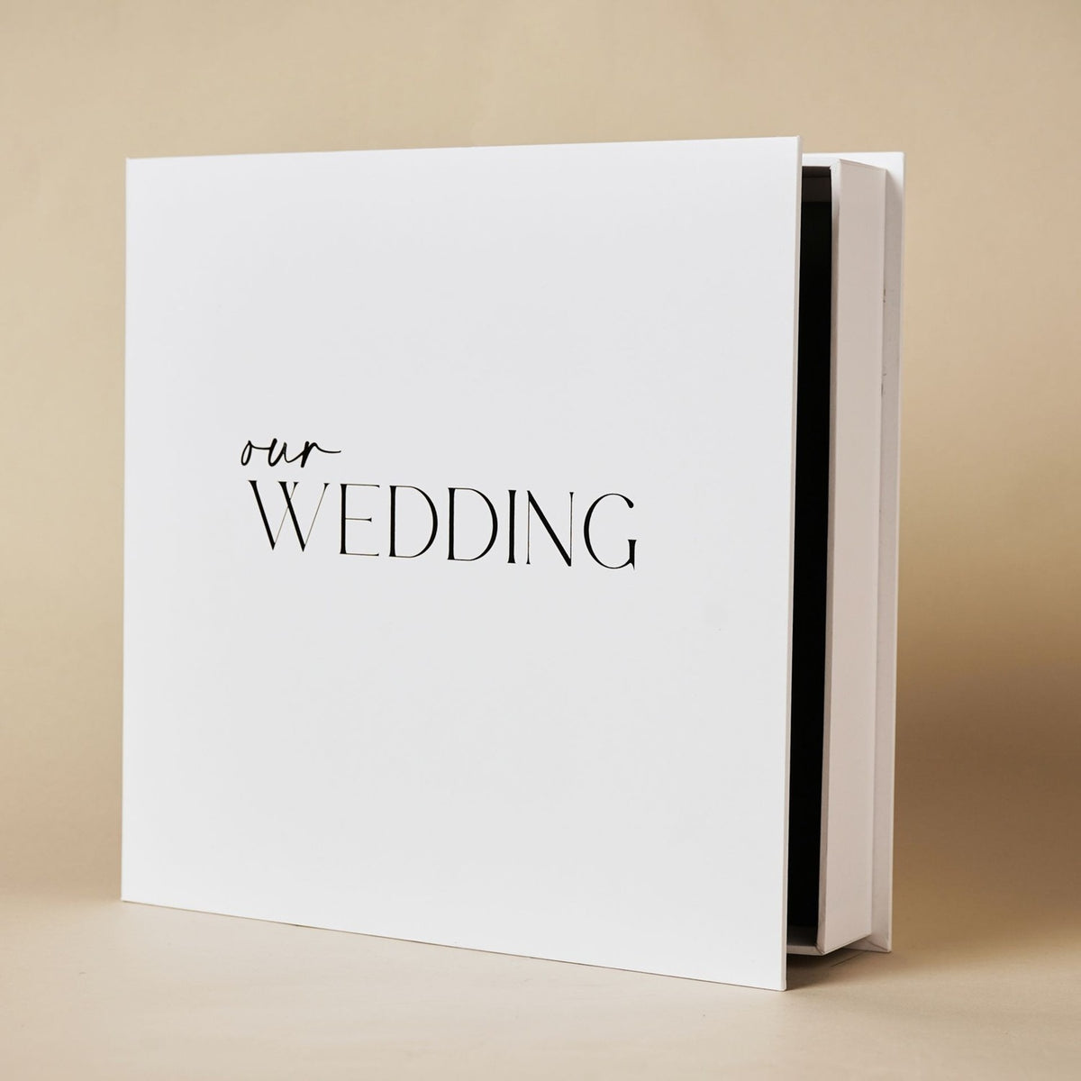 Square white "Our Wedding" photo album in matching box, with 'our' in script and 'WEDDING' in capitals, shown at an angle on a plain background.