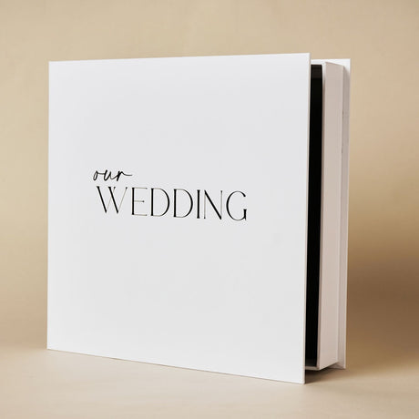 Square white "Our Wedding" photo album in matching box, with 'our' in script and 'WEDDING' in capitals, shown at an angle on a plain background.