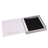 White square photo album open in its matching box, showing black pages bound with two screw posts, "happily ever after" printed on the inner cover, set against a plain white background.