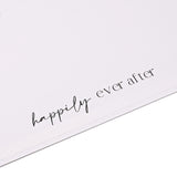 Close-up of the white square coffee table photo album's corner, showing "happily ever after" printed in black script across the cover.