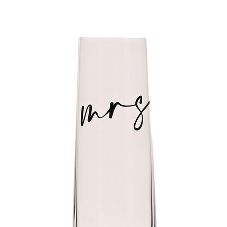 Close-up of a clear stemmed champagne flute showing "mrs" in black lowercase script across the glass, set against a plain white background.