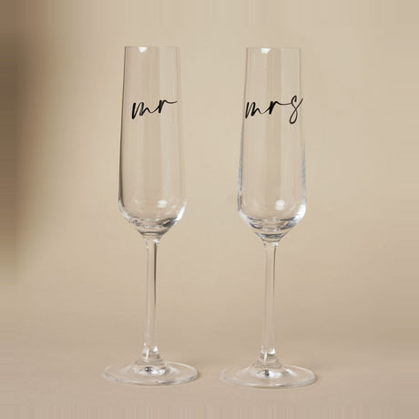 Set of 2 clear champagne flutes with "mr" and "mrs" in black lowercase script on tall, narrow bowls and slender stems, shown on a plain neutral background.