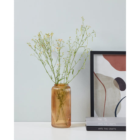 Ambalabe ribbed amber glass vase with wildflower stems, styled on a table beside an abstract framed print and stacked books against a light wall.