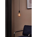 Amber Dimmable LED Globe Bulb E27 G125 glowing warmly on a black pendant cord above a navy armchair in a muted pink room setting.