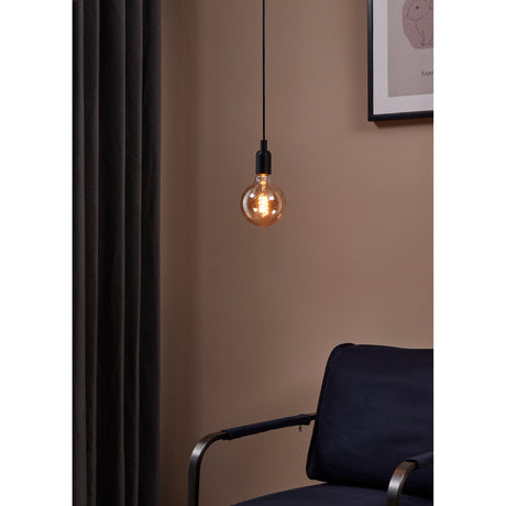 Amber Dimmable LED Globe Bulb E27 G125 glowing warmly on a black pendant cord above a navy armchair in a muted pink room setting.